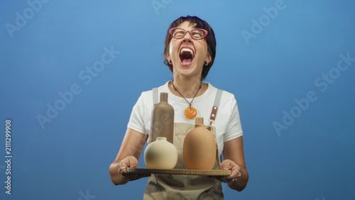 Foto Woman holding a tray of pottery vases, hands visible, mouth open shouting in studio; creative celebration joy