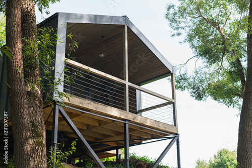 house stands elevated among trees, showcasing a sturdy wooden deck and large openings. The scene captures the blend of architecture and nature, inviting outdoor living
