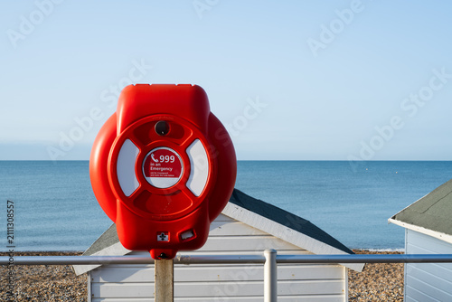 Фотография Emergency lifebuoy housing with 999 rescue information overlooking a pebble beac