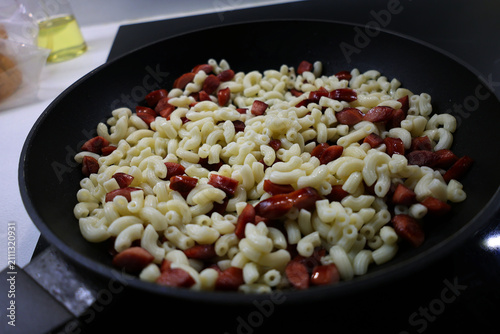 View of pasta with sausage pieces being heated in a pan, frying food in a pan, close-up on food
