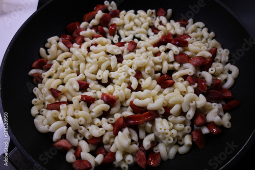 View of pasta with sausage pieces being heated in a pan, frying food in a pan
