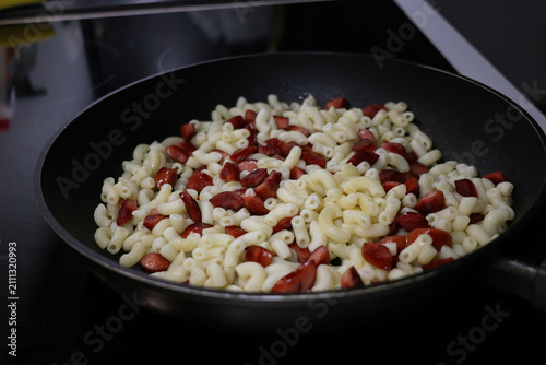 Pasta with pieces of sausages is heated in a frying pan, frying food in a pan
