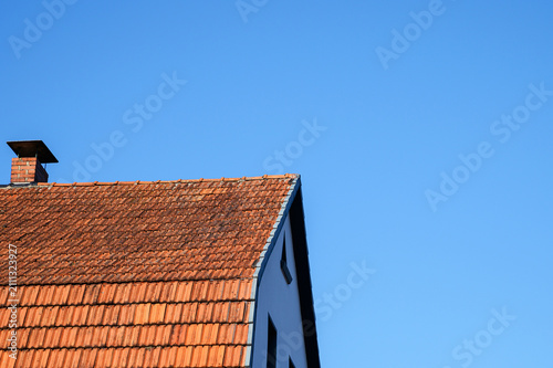 Old terracotta tiled roof with brick chimney against a clear blue sky