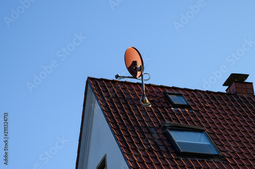 Red tiled house roof with satellite dish skylights and chimney against blue sky