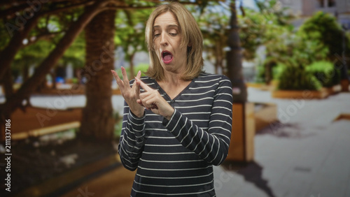 Foto Woman inspects a fingernail on her hand in a busy street plaza, using the other hand to point and closely examine a possible hangnail or small injury; disgust concern