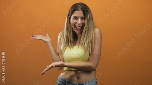 фотографія Woman points fingers and grins, showing hands and exposed midriff in a studio pointing pose; cheerful invitation