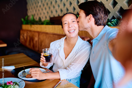Foto Cheerful couple sharing a meal, man kissing woman's cheek while she smiles at th