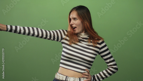 Photography Woman points finger left with outstretched arm, index finger visible, wearing black and white striped crop top and studded belt against a green studio backdrop; accusation anger