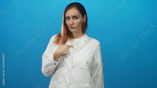 Fotografie Woman in white coat points finger to chest in studio and later raises index with a clenched hand, conflicted expression; apology