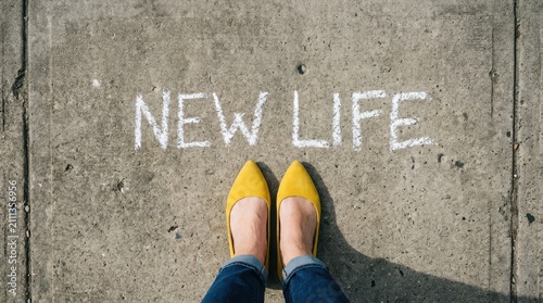 Persons feet standing on concrete pavement with new life written in chalk, symbolizing a fresh start
