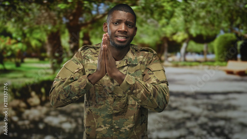 Fotografie Man soldier pressing hands together in prayer gesture showing palms and fingers in forest path with bench behind; duty honor hope resilience