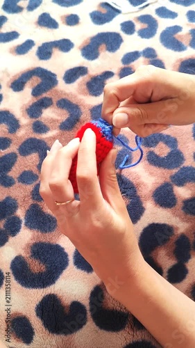 Person holding handmade knitted heart craft, hands holding red yarn heart with blue detail, handicraft hobby.