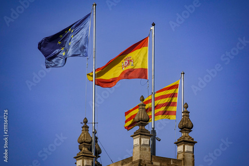 Flags of the European Union, Spain and Catalonia flying above a historic building in Barcelona.