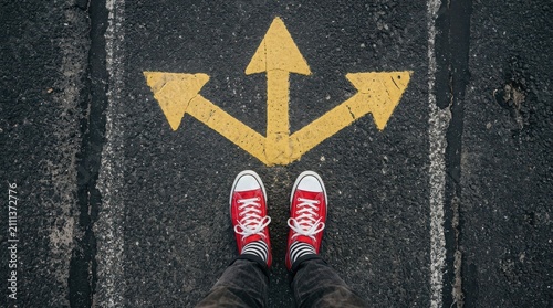 Person standing on asphalt road with yellow painted arrows pointing in three different directions