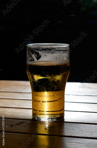 A glass of beer on a table illuminated by sunlight.