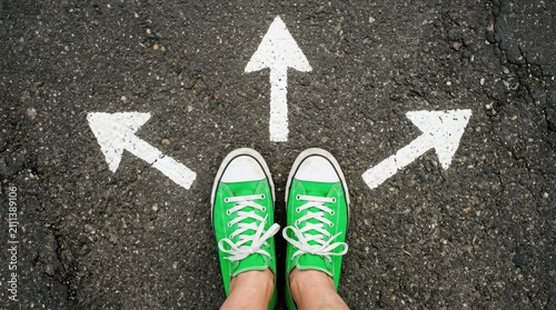 Person wearing green sneakers standing at a crossroads with three white arrows