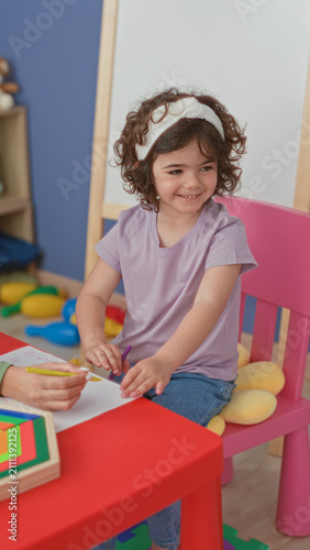 Fotografía Little girl drawing with purple marker, hand on paper at red table and pink chair in building; playful creativity