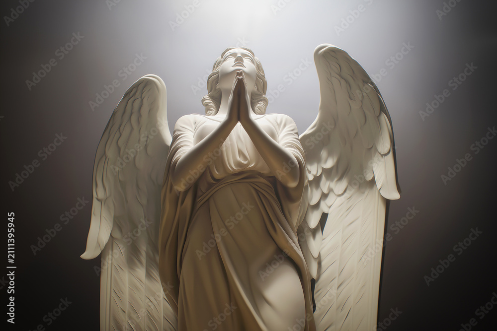 Obraz premium A marble angel statue stands with hands clasped in prayer beneath a moody sky. Spiritual guardian of faith, devotion, hope, protection, memorial, serenity and religious art. Funeral, burial.
