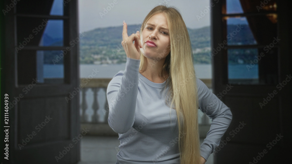 Fototapeta premium Woman points finger at camera from a balcony doorway in building, hand on hip and stern face; firm disapproval.