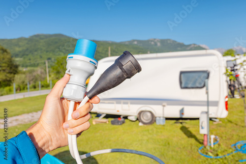 Φωτογραφία Hand holding electric hookup cable connectors at campsite with caravan