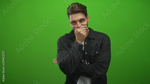 Foto Hispanic man with beard covering mouth with hand and crossed arm, in a green screen studio; amused reflection