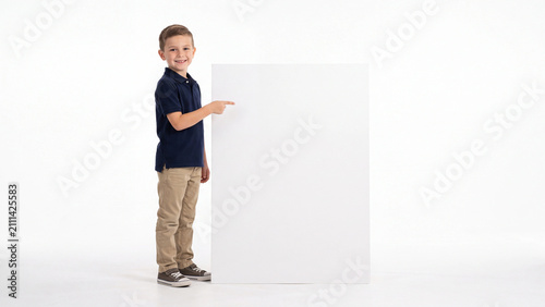 Schoolboy points toward a large white rectangular board that provides substantial copy space for custom promotional messaging or educational announcements in a studio setting.