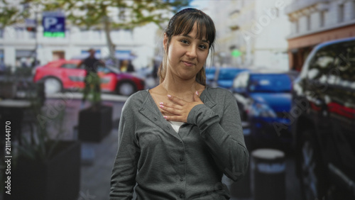 Foto Woman hand on chest gesture in street with parked cars, planters and building facades; gratitude sincerity