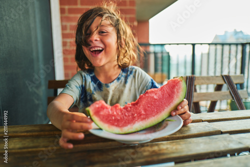 Photography Boy holding up a watermelon slice at a balcony table