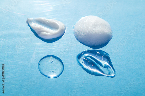 Skincare gel, cream, foam and serum texture samples on blue background, cosmetic product drops