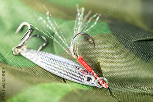 Quadro em tela Silver fishing lure on camouflage fabric The Concept of outdoor sports