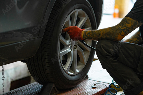 Mechanic's tattooed hand inflating car tire valve