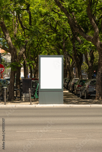 Foto Blank vertical billboard mockup installed along a tree-lined urban avenue with parked cars in the background
