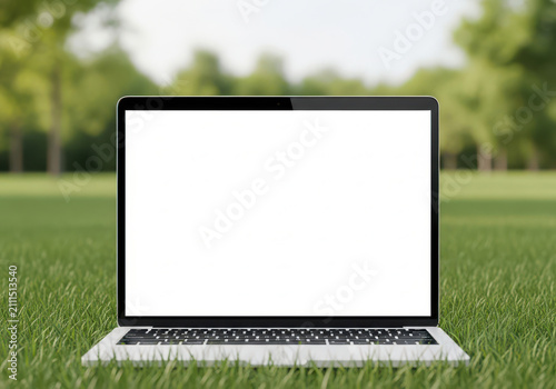 A modern laptop with a blank white screen placed on green grass