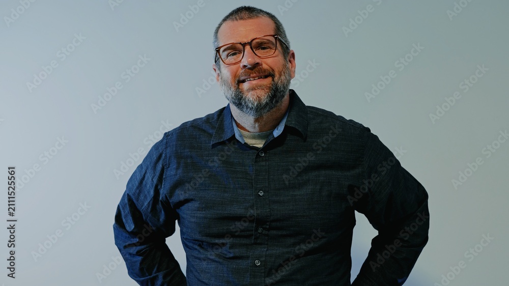 Fototapeta premium Confident middle-aged man with beard wearing a dark button-down shirt posing against a neutral backdrop, representing modern business leadership