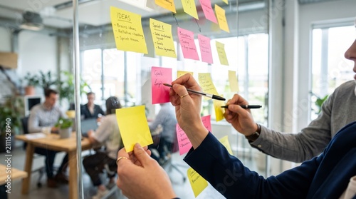 Agile Project Management Team Writing Strategy and Sprint Goals on Sticky Notes in Glass Office Wall