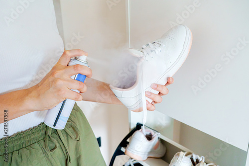 Obraz na płótnie Close-up of a woman using hygiene aerosol spray deodorant for sneaker care and protection inside a minimalist apartment