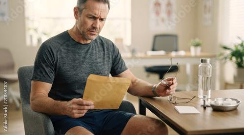Middle-aged man in a clinic consultation room after hormone testing, holding lab results beside a blood draw tray, water bottle, and appointment card.