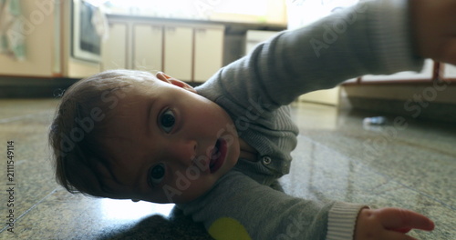 Obraz na plátně Casual authentic scene of baby infant on kitchen floor wanting to touch camera l