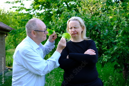 caring grandfather invites his grown daughter to taste freshly harvested lettuce from garden. food preferences create a lighthearted family moment centered on healthy nutrition and natural produce.