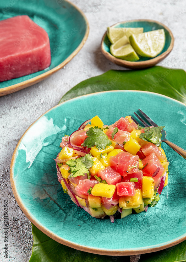 Obraz premium Tropical style gourmet tuna mango salad tartar with cilantro and purple onion. On blue plate, tropical leaves