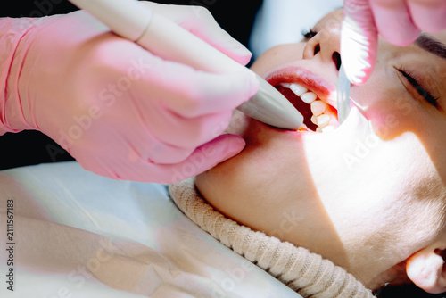 A dentist wearing gloves removes plaque from an ultrasonic scaler.
