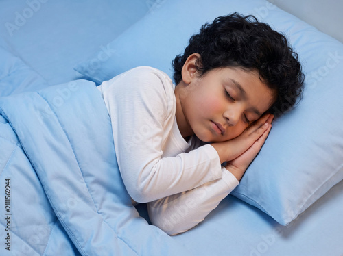 young fair skinned indian boy peacefully sleeping on luxury sky blue bedding at night in side profile representing healthy child sleep parenting pediatric wellness and bedtime routine