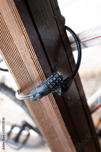 Obraz na płótnie A close-up view shows a black combination cable lock secured around a bicycle frame and a wooden post