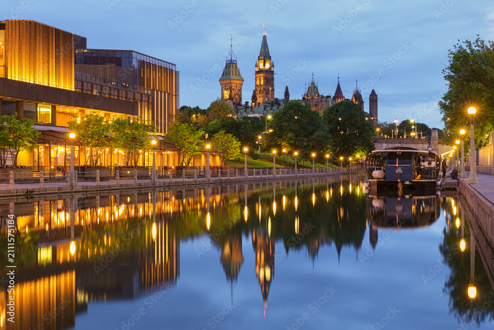 Obraz premium Evening view of the Rideau Canal in downtown Ottawa, Canada, with illuminated waterfront buildings, city lights and colorful reflections on the calm water