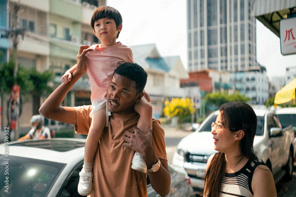 Obraz premium Diverse family enjoying urban stroll, father carrying child on shoulders