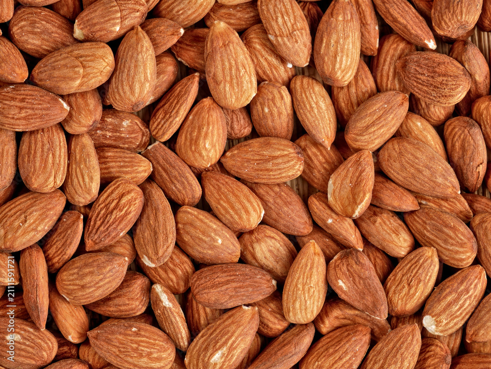 Fototapeta premium A close-up, overhead view of a large pile of raw almonds. The nuts are brown and oval-shaped, with visible texture on their shells.