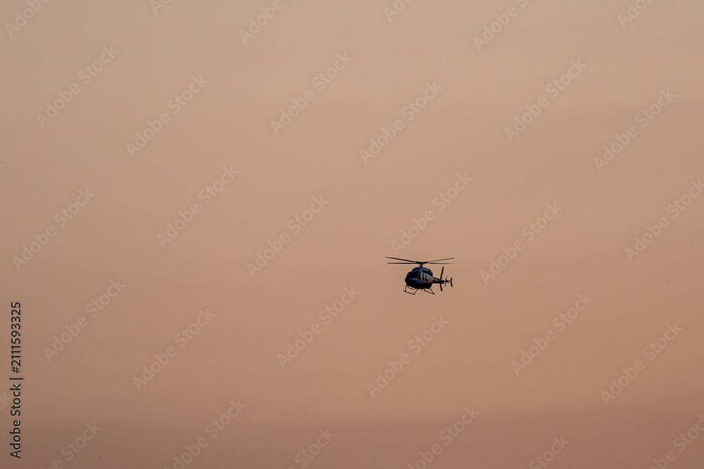 Fototapeta premium Sunset Helicopter Flying Through the Evening Sky. Helicopter Silhouette Against a Colorful Sunset Sky. Golden Sunset Sky Featuring a Flying Helicopter.