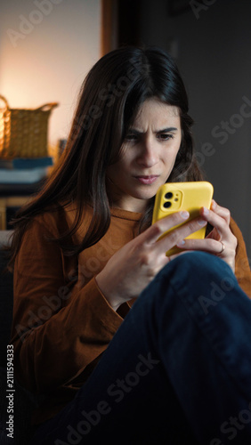 Canvastavla Young Hispanic woman sitting on her sofa straining her eyes to see her smartphone, representing vision problems, digital eye strain and excessive screen use