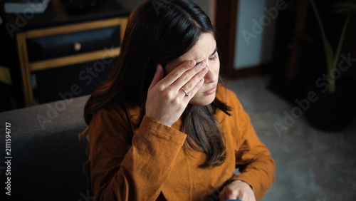 Konstfotografi Young Latina woman sitting on her sofa with an itchy eye caused by digital eye s