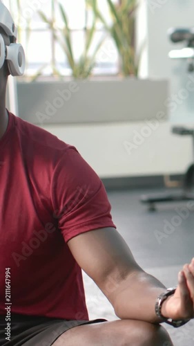 Vertical video: Cooling down man holding calm pose on gym mat with red tee, headphones, copy space